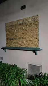 Residential window boarded up at night, OSB fitted flush above the sill